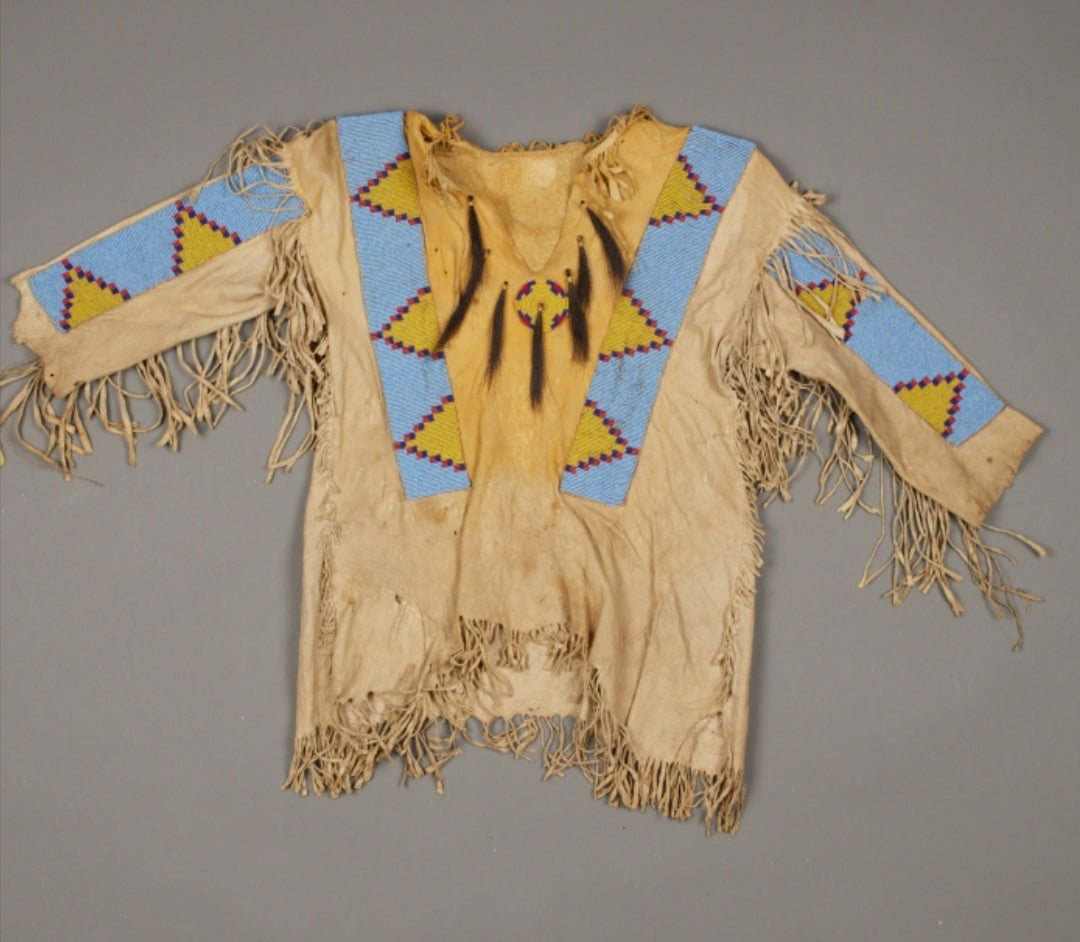 Traditional Native American garment with fringes and geometric patterns on a gray background