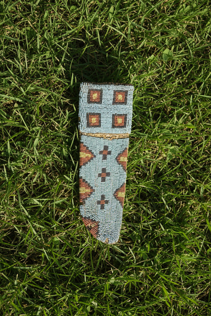 Decorative beaded knife sheath with geometric pattern on a white background