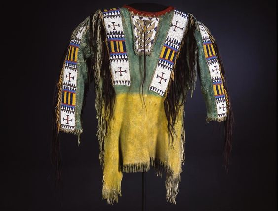Traditional Native American garment with intricate patterns and fringes on a dark background