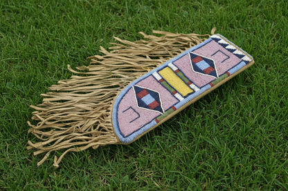 Decorative knife sheath with beadwork and fringes on a gray background