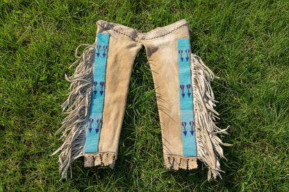 Pair of fringed leather leggings with blue bands and arrow designs on a white background