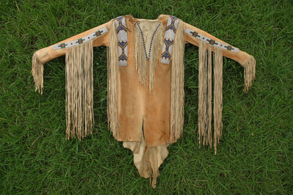 Traditional Native American War Shirt with fringes and bead work on a Grassy background