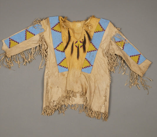 Traditional Native American garment with fringes and geometric patterns on a gray background