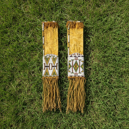 Two decorative leather strips pipe bags with beadwork and fringes on a grass background