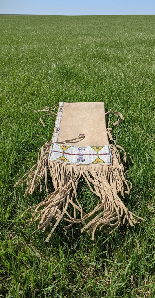 Beige fringe bag with a colorful pattern on a grassy field